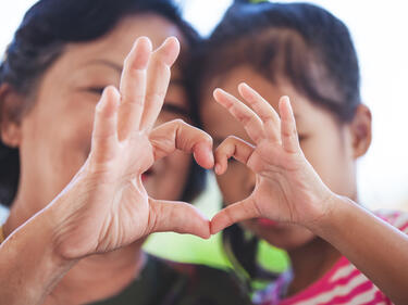  grandmother and little child girl making heart shape with hands together with love