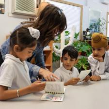 Female Teacher and three male elementary students look at their new books