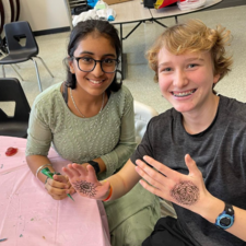 Two students smiling and one showing off the Henna done on their hand