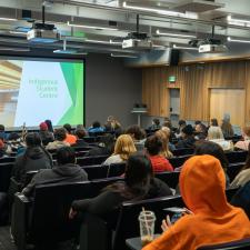 Large group of students gathered in large room in seats listening a speaker