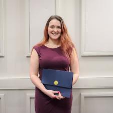 Female ABC award recipient stands in front of wall holding certificate