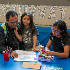 Parent and two students sitting at a school table looking at school work